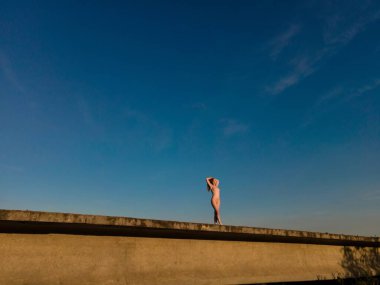 Güneşli bir günde beton köprüde duran ve bulutsuz mavi gökyüzüne doğru uzun saçlara dokunan fark edilemeyen, çıplak bir kadın.