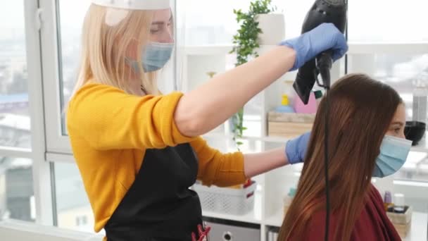 Kapsalon in masker zorgt voor het haar van de klant met haardroger — Stockvideo