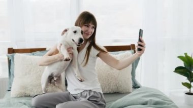 Yatağında telefonu ve köpeği olan bir kız.