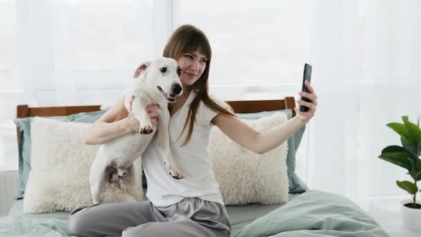 Девушка с собакой и телефоном в кровати — стоковое видео