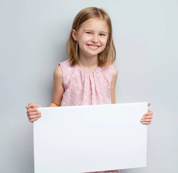 Okullu kız elinde boş beyaz poster tutuyor. — Stok fotoğraf