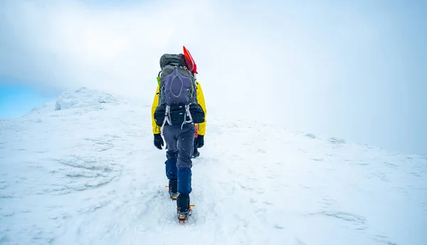 Uomo a piedi verso la cima della montagna innevata — Foto Stock