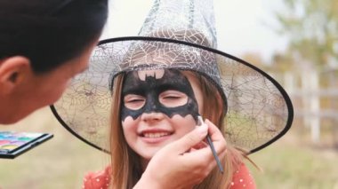 Mother painting art on girl for halloween