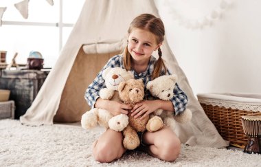Küçük kız peluş ayıcıkları kucaklıyor ve gülümsüyor.