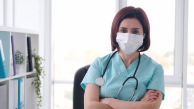 Klinikte durup kameraya bakan maske takan güzel kadın portresi. Coronavirus zamanında hastanede tıp uzmanıymış. Mavi üniforma ve koruma giyen doktor.
