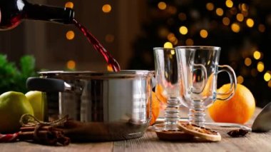 Şarap hazırlamak için arka planda Noel arifesi ışıkları olan kırmızı alkolü şişeden tavaya döker. Tatil akşamında baharatlı geleneksel sıcak içecek.