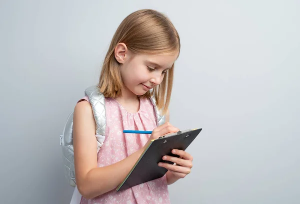 Mała Dziewczynka Robi Notatki Ołówkiem Stojącym Pod Szarą Ścianą — Zdjęcie stockowe