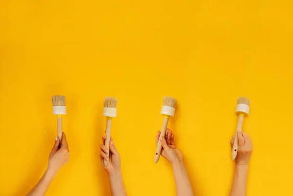 Four Hands Holding Paint Brushes Yellow Background Copy Space Concept — Foto Stock