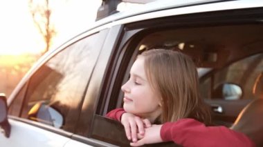 Preteen girl in the moving car looking from window outside and smiling. Pretty kid in vehicle transportation