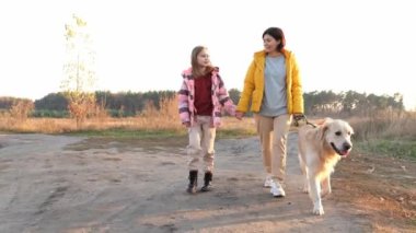 Girl and her child with golden retriever dog walking and talking in sunset time at nature. Mother with daughter and doggy pet outdoors