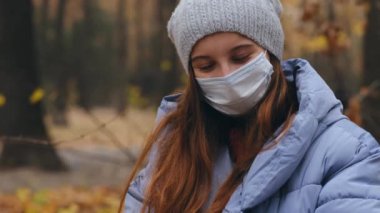 Sonbahar parkında yürürken koruyucu maske takan genç bir kız.