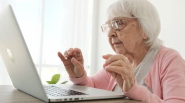 Dizüstü bilgisayarla çalışmak için gözlük takan yaşlı bir kadın. Modern teknolojileri keşfeden yaşlı kadın.