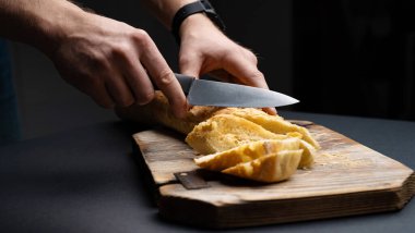 Fransız ekmeği bruschettalar için. Kadın eli tarafından tahtadan yapılmış bıçakla kesilmiş. Çerezler için dilimlenmiş kabuklu mısır ekmeği.
