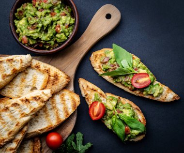 Tahta tahtada roka ile servis edilen guacamole, fesleğen ve vişneli domatesli yumurtalı ekmek. Meksika antipasti dilimli ekmek, avokado püresi, otlar ve sebzeler.