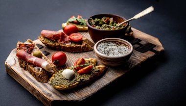 Jambonlu bruschetta, zeytin, pesto, domates ve fesleğen, ahşap tahtada guacamole ve otlu tuz ile servis edilir. Akdeniz antipastası ile şık besin bileşimi