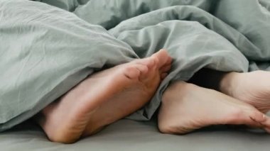 Uykudan sonra birlikte vakit geçiren mutlu çift ayakları. Kadın ve erkek ayakları yatakta battaniyenin altında. Sabahları karı ve kocanın bacakları birlikte.