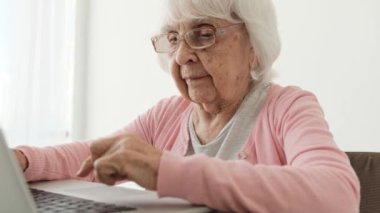Dizüstü bilgisayarda yazı yazan son sınıf öğrencisi bir kadın. Evde yavaş yavaş. Yaşlı kadın defter tuşlarına basıyor ve ekrana bakıyor