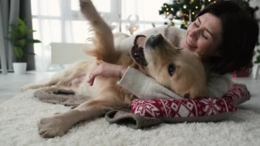 Yeni yıl süsü ve gülümsemesiyle evde Golden Retriever köpeğini okşayan bir kız. Xmas 'ta evcil köpeği olan genç bir kadın.