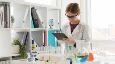 Korunma gözlüğü takan liseli kız kimya dersinde labaratuarda notlar alıyor. Laboratuvarda ekipmanla çalışan bir kız öğrenci.