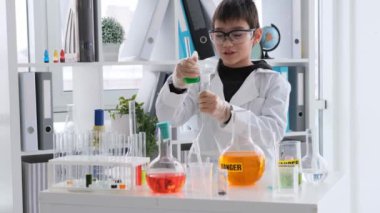 Kimya dersindeki öğrenci kimyasal sıvılı şişeleri anlatıyor. Öğrenci çocuk laboratuarda çalışıyor ve deneyler yapıyor.