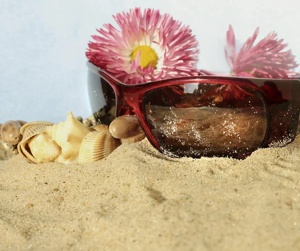 太阳镜配件和鲜花在沙子里 — 图库照片