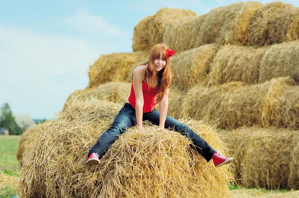 Gelukkig lachend jong meisje, zittend op een hooi — Stockfoto