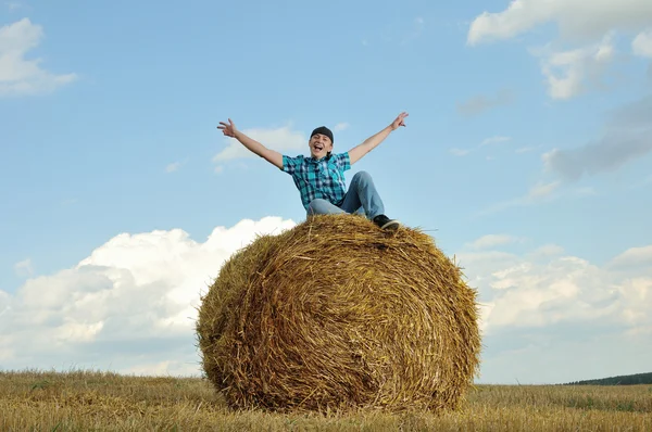 Man on a stack of straw against a field — Stock Photo, Image