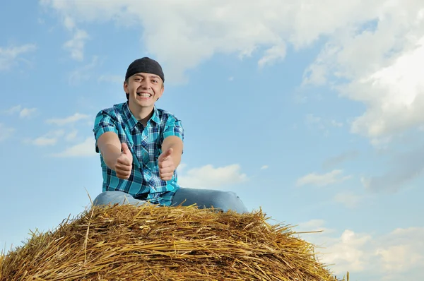 Man on a stack of straw against a field — Stock Photo, Image