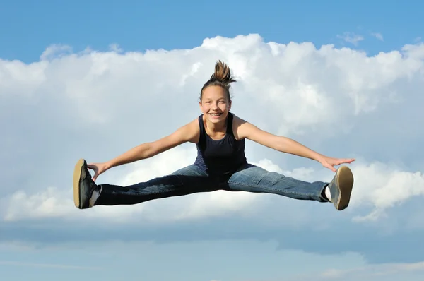 Beautiful girl in gymnastic jump against blue sky — Stock Photo, Image