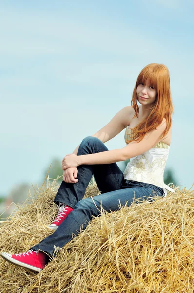 Gelukkig lachend jong meisje, zittend op een hooi — Stockfoto