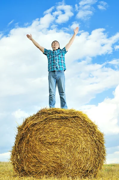 Man on a stack of straw against a field — Stock Photo, Image