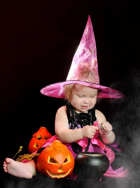 Halloween bébé sorcière avec une citrouille sculptée sur fond noir — Photo