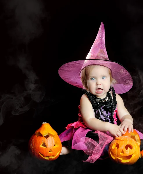 Halloween baby witch with a carved pumpkin over black background Stock Photo