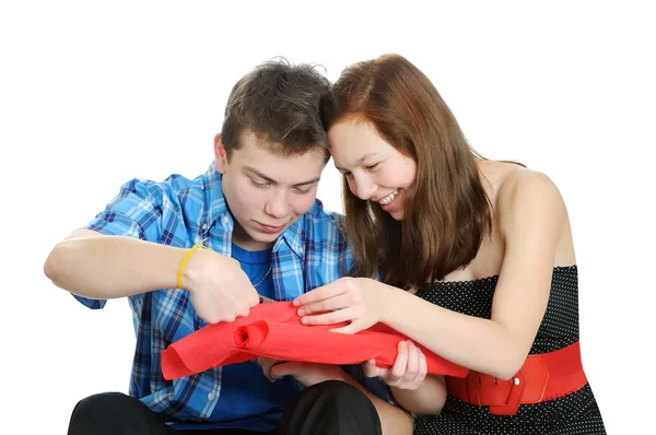 Smiling teenage girl and boy cutting valentine heart out of red paper with scissors over white background — Stock Photo, Image