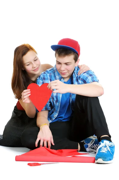 Sorrindo adolescente e menino segurando um valentine cortado a partir de papel vermelho com tesoura sobre fundo branco — Fotografia de Stock