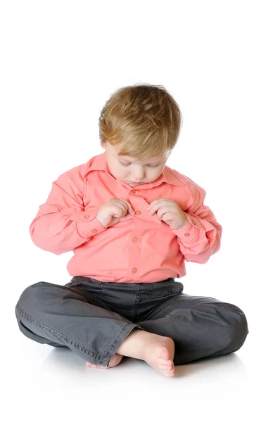 Roztomilý chlapeček sedí na podlaze a na tlačítko při pohledu na tričko — Stock fotografie
