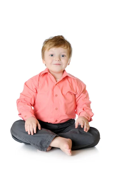 Adorabile ragazzino sorridente, seduto sul pavimento, girato in studio, isolato su sfondo bianco — Foto Stock