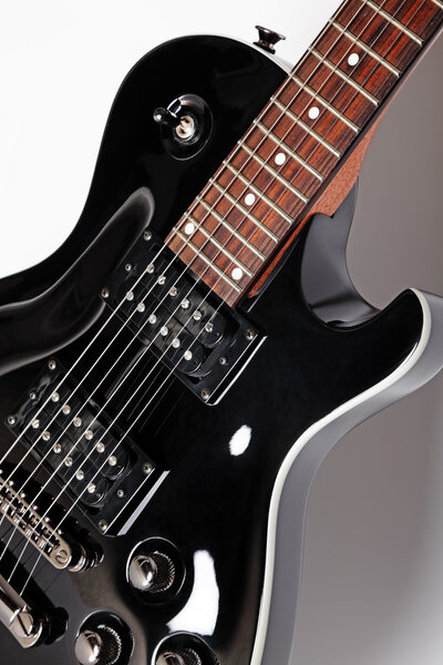Black electric guitar close-up on a grey background, studio shot