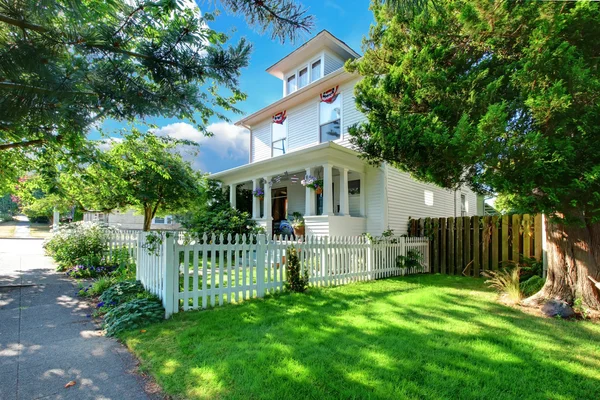 White historical American house with porch fence and green grass.