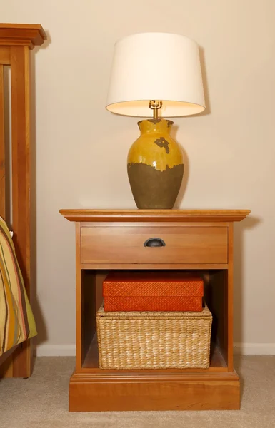 Table de chevet en bois avec lampe et lit . — Photo