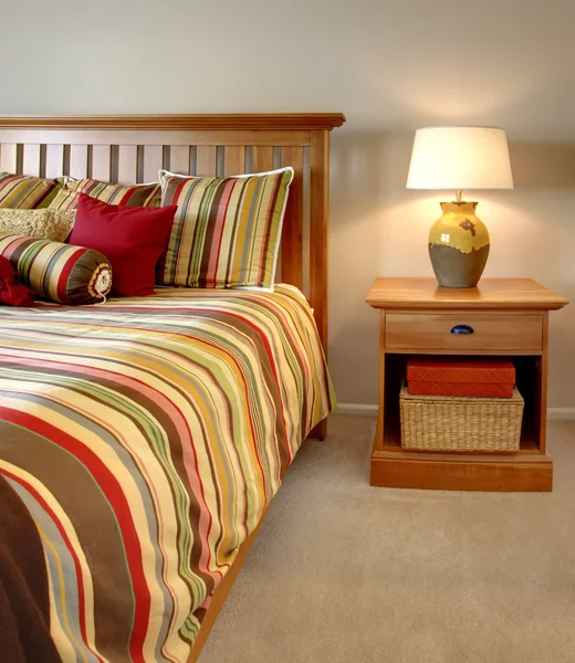 Cama de madera y mesita de noche con rayas en rojo, amarillo y verde . — Foto de Stock