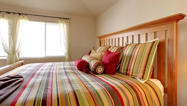 Большая кровать с красивым постельным бельем в полоску красного, желтого и зеленого цвета . — стоковое фото