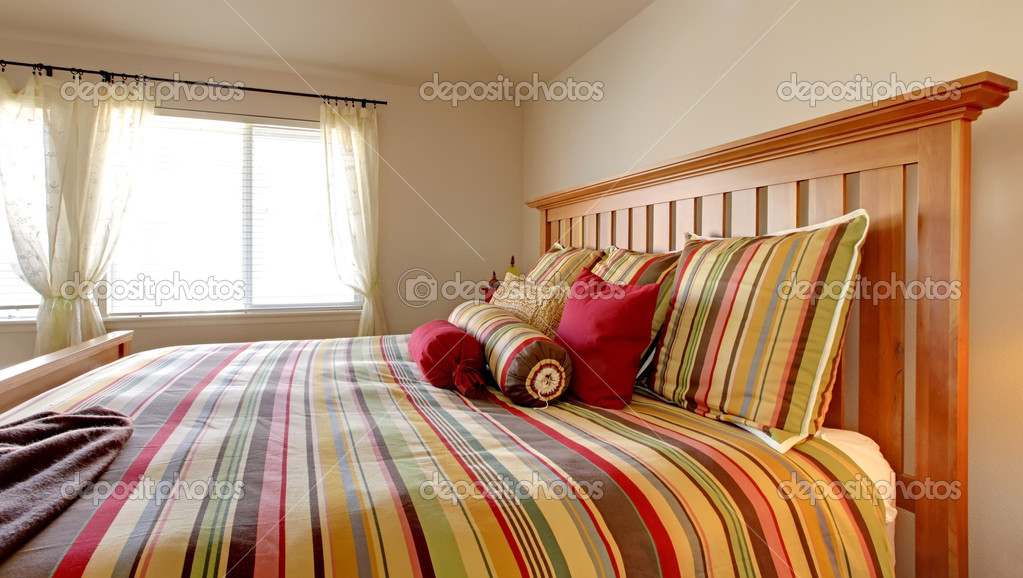 Large bed with beautiful bedding in stripe red, yellow and green. ⬇