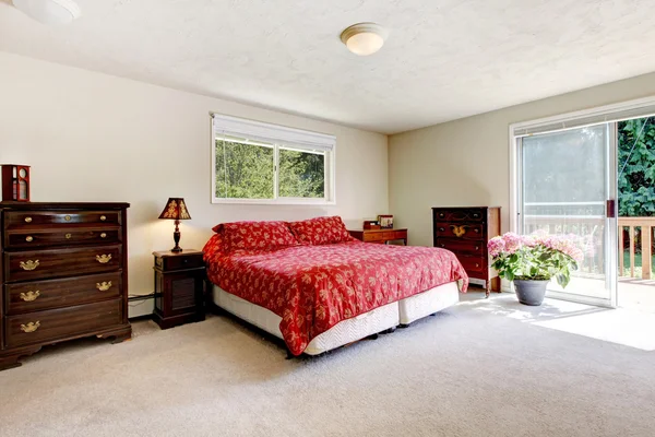 Bedroom with red bed, open balcony door and beige walls. — Stok fotoğraf