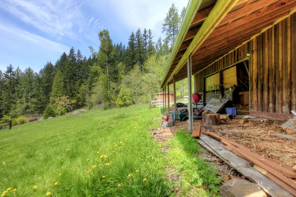 Old large shed with green spring landscape and fence. — Stock Photo, Image