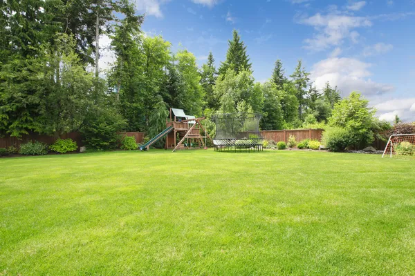 Summer fenced backyard with play ground area and trees. — Stock Photo, Image