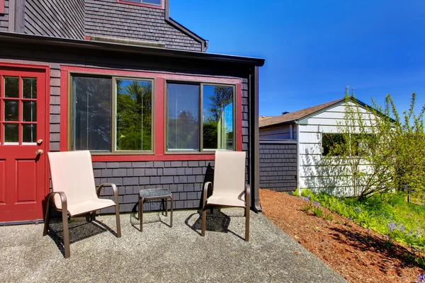 Twee stoelen naast rode deur en kleine zwart huis. — Stockfoto