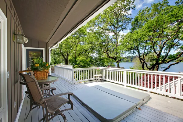 Duży balkon długi na zewnątrz domu z wanną z hydromasażem i krzesła, widok na jezioro. — Zdjęcie stockowe