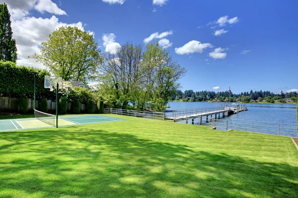 Tennis court with lake and bright green grass. — Stock Photo, Image