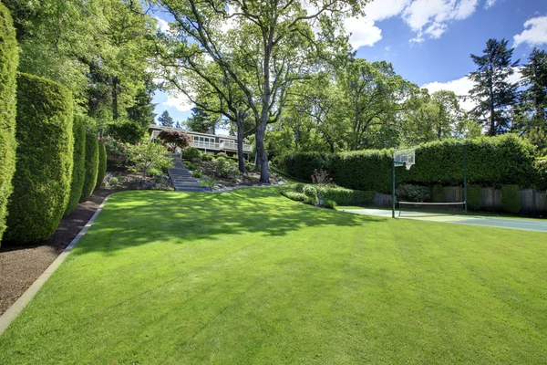 Pista de tenis con casa en la colina y hierba verde brillante . —  Fotos de Stock